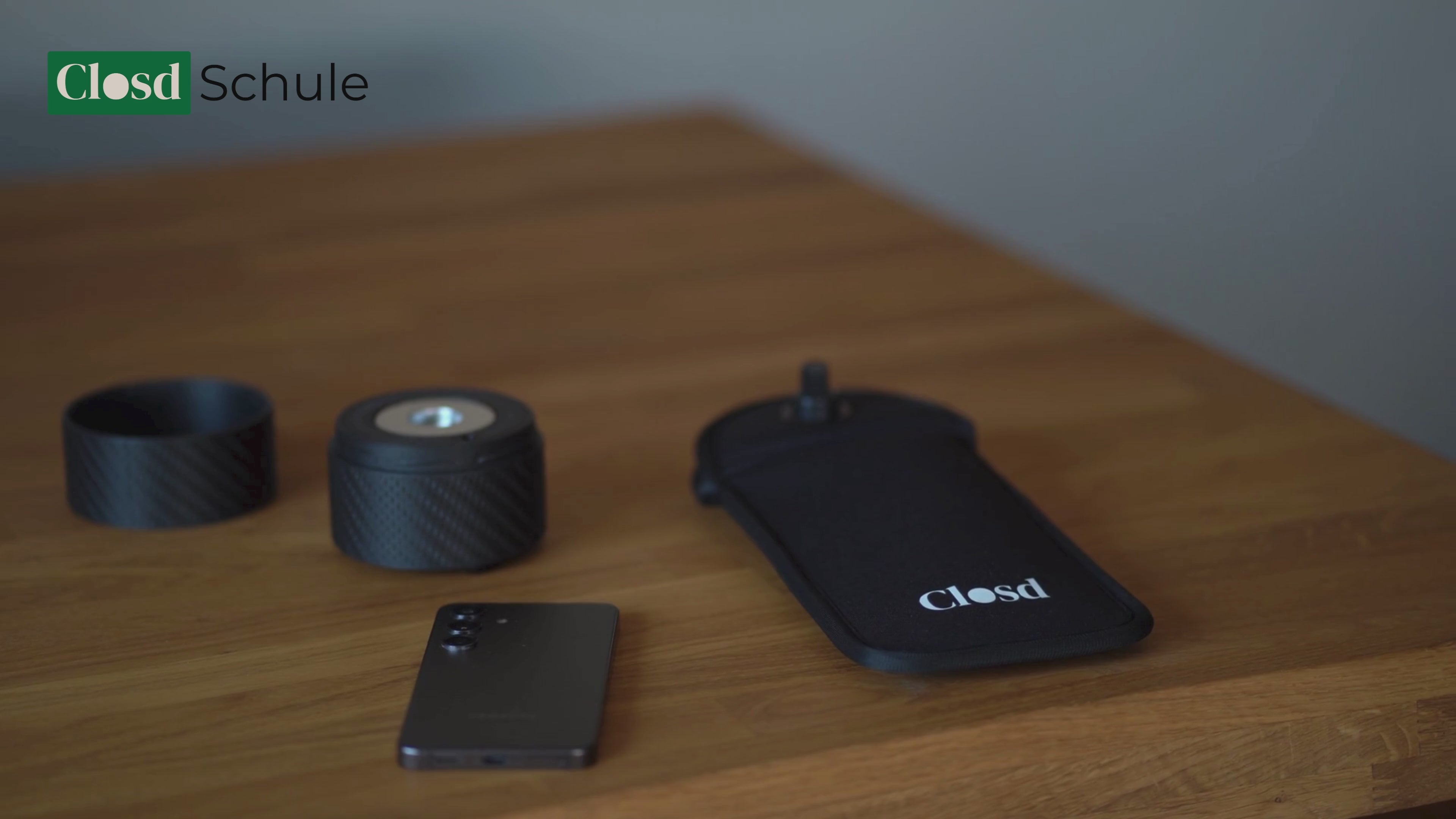 Video laden: Das Handy wird in die geöffnete Handytasche eingelegt. Eine Person verschließt die Handytasche über das Drücken eines Knopfes. Die Handytasche ist jetzt verschlossen und kann nicht mehr von Schülerinnen und Schülern geöffnet werden. Die Handytasche wird durch das Auflegen auf einen Magnetöffner geöffnet.